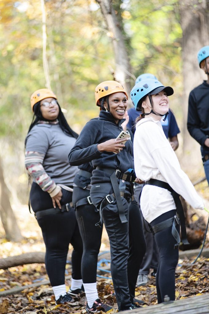 Three women smiling in their climbing helmets during their Outward Bound teambuilding program