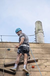 A man reaches the top of a rockwall during a professional teambuilding day and looks down to his team below.